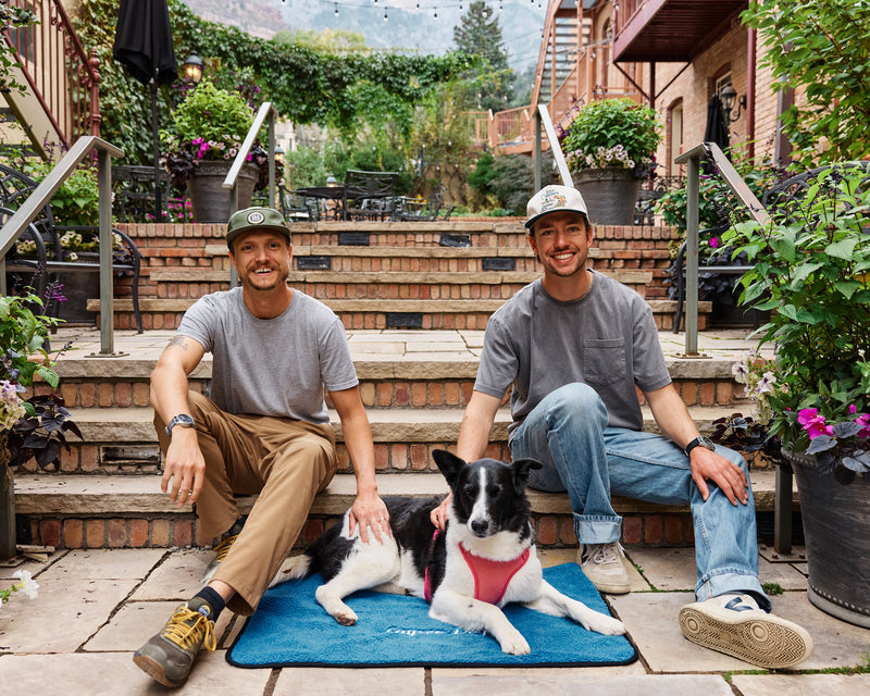 Two men sitting at a restaurant with a dog on the My Place portable dog bed in Colorado Sky.