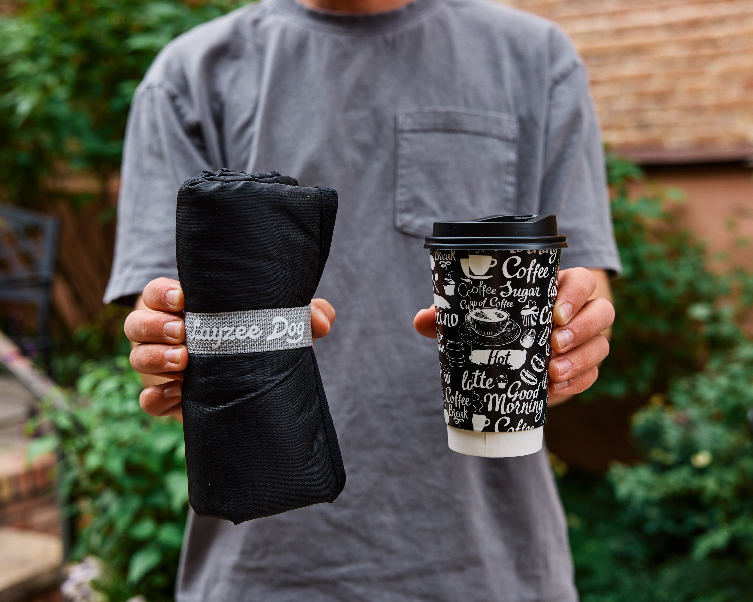 A person holding a rolled up My Place portable dog beg and a cup of coffee showing that they are a similar size
